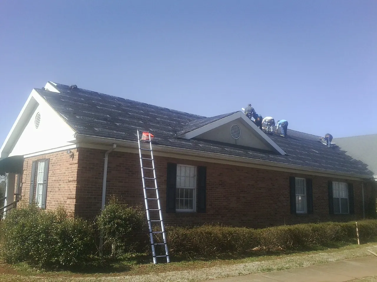 Crew tearing shingles off a brick ranch roof with a ladder set — Emergency Roof Repair work by our crew in Kennedy