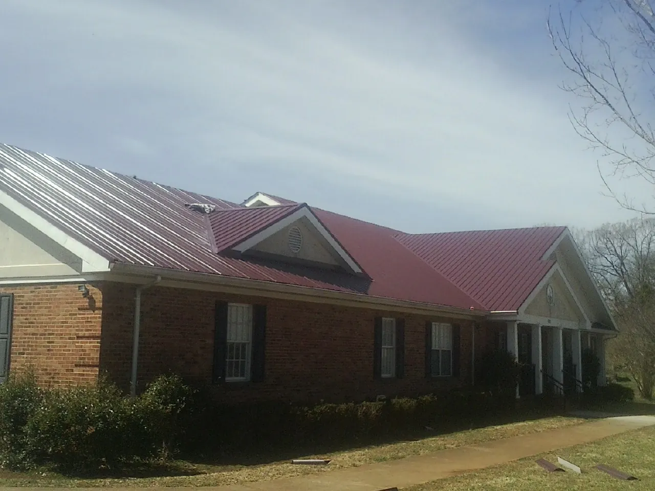 Red metal roof with gabled entries on a long brick building, from a Hail Damage Roof Repair job in Kennedy