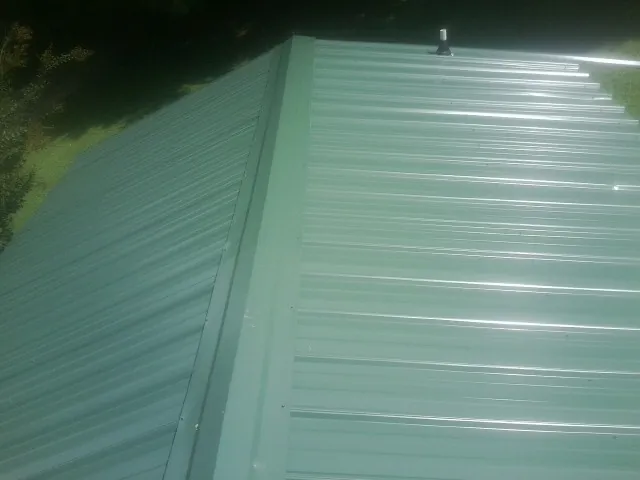 New green metal panels meeting at the ridge of a roof — Flat Roof Repair work by our crew in Kennedy