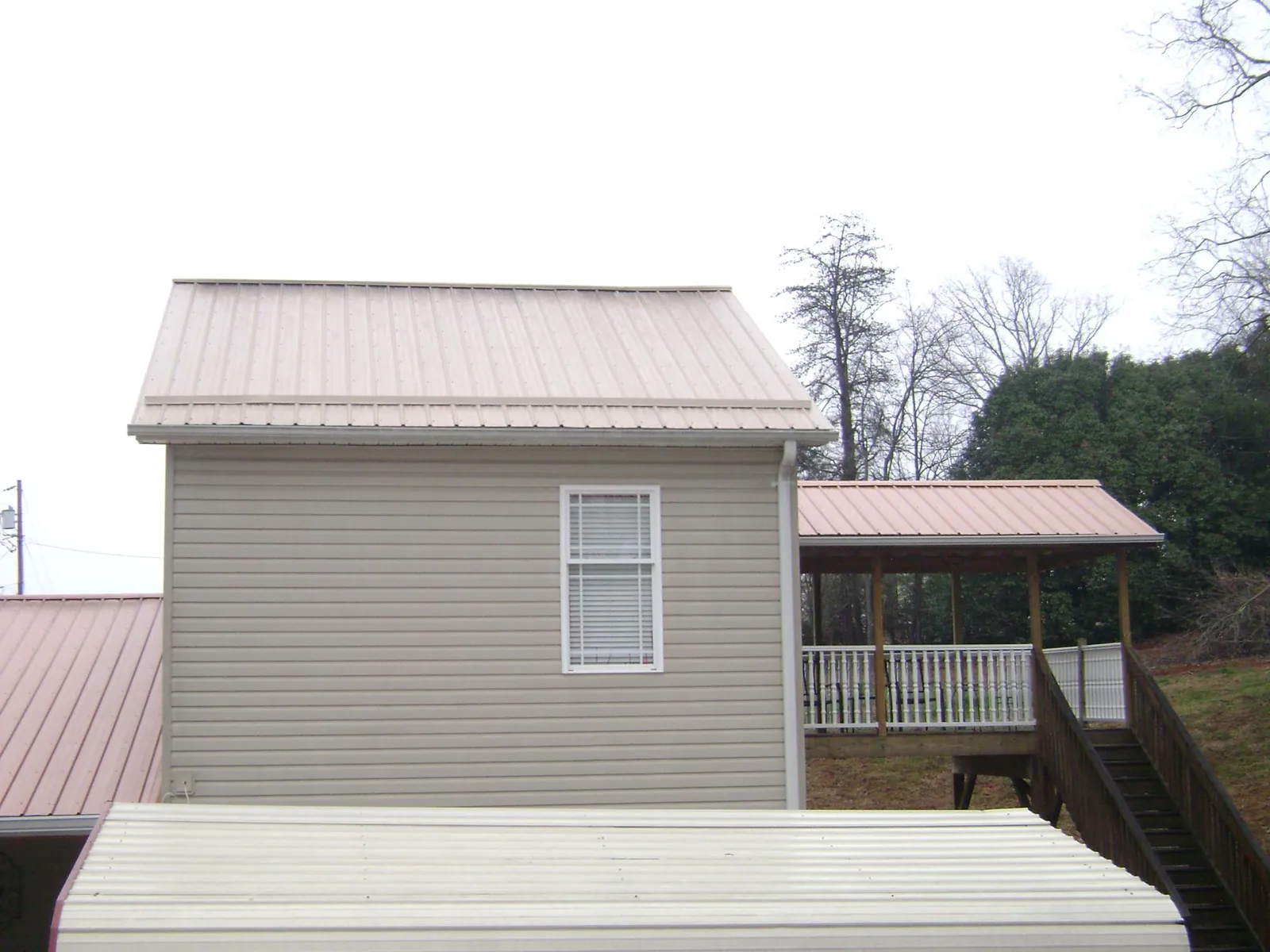 Tan metal roofs on a two story addition and attached porch, from a Roof Replacement job in Kennedy